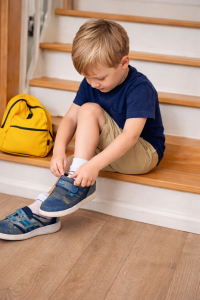 Boy putting on his own shoes while sitting on stairs