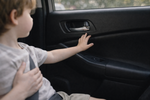 Child reaching toward a car door handle while an adult stops them