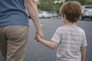 Adult and child holding hands while walking in a parking lot near parked cars